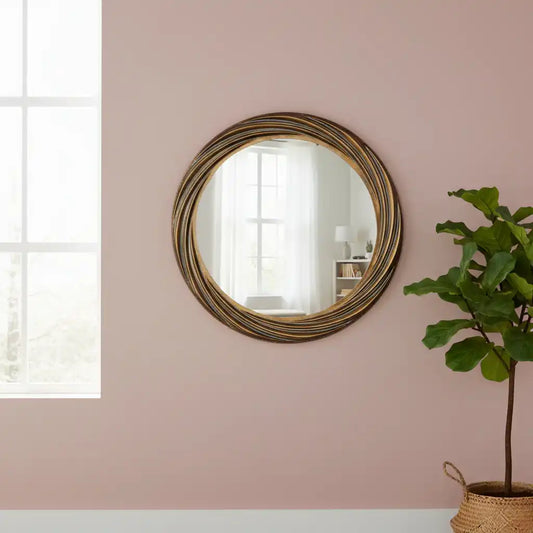 Round gold-framed mirror on a pink wall with a plant in the foreground