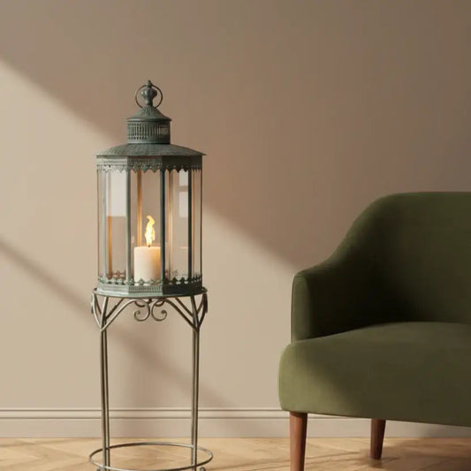 Decorative lantern with a candle on a stand next to a green armchair in a room.