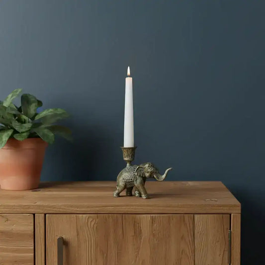 Decorative elephant candle holder with a candle on a wooden surface against a dark blue wall.