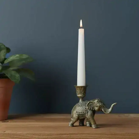 Bronze elephant candle holder with a lit white candle on a wooden surface against a dark blue wall.