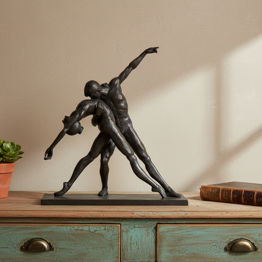 Bronze sculpture of two figures on a wooden surface with a plant and book in the background