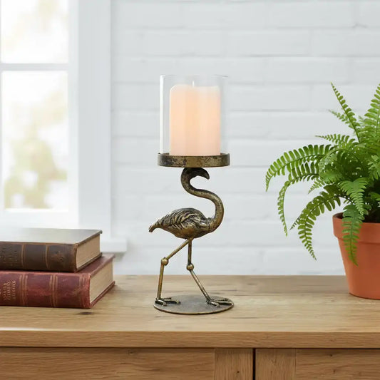 Bronze flamingo candle holder with a candle on a wooden surface against a stone wall.