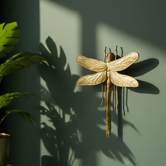 Gold dragonfly wall decoration on a green wall with plant shadows