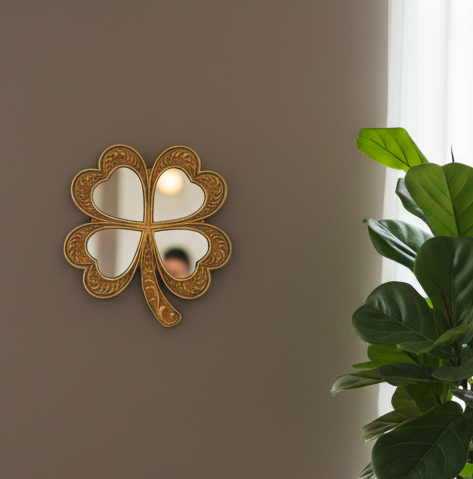 Decorative four-leaf clover mirror on a wall with a plant in the corner