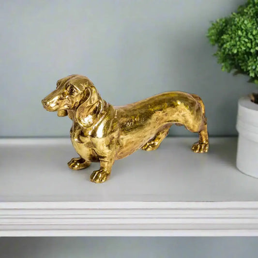 Gold dachshund figurine on a white surface with a light gray wall and green plant in the background