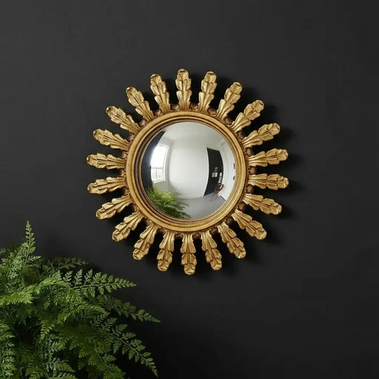 Decorative gold sunburst mirror on a black wall with a plant in the foreground.
