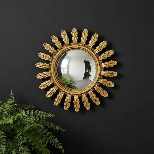 Decorative gold sunburst mirror on a black wall with a plant in the foreground.