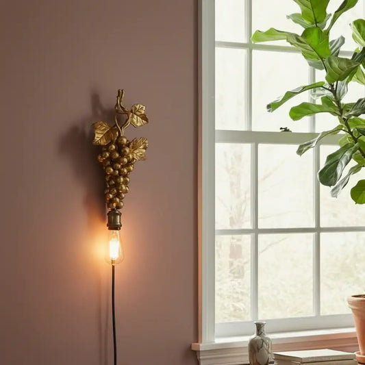 Decorative wall light with grape design next to a window with a plant