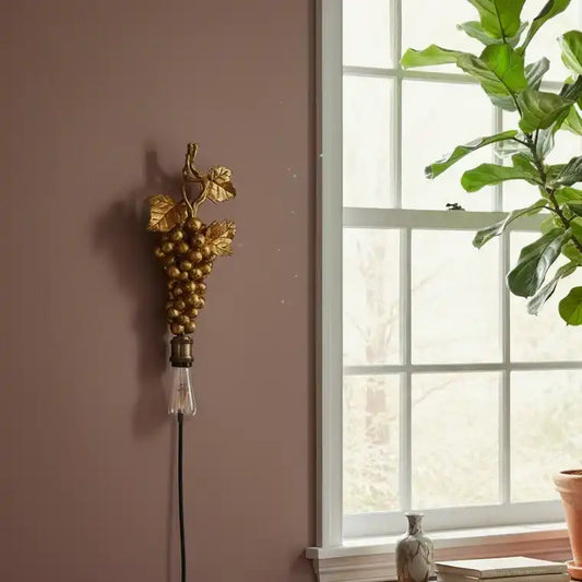 Decorative wall sconce with grape design on a wall next to a window with a plant.