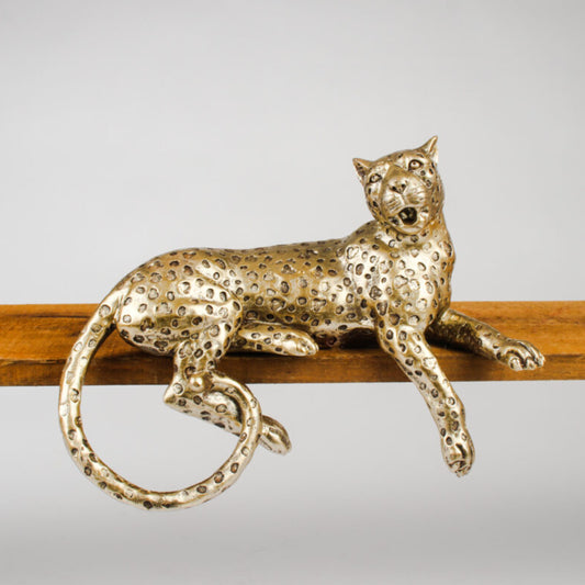 A metallic leopard figurine with a textured, speckled gold finish, resting on a wooden bar against a neutral gray background.