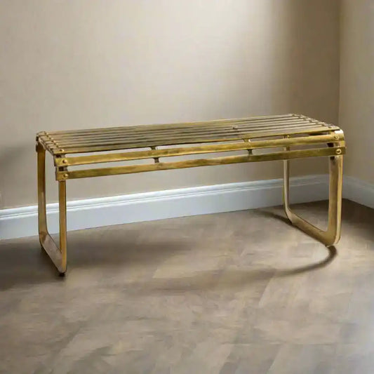 Gold metal bench against a plain wall on a wooden floor