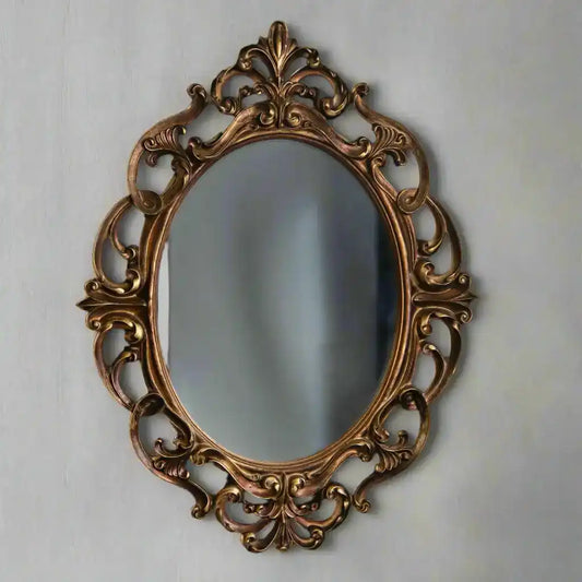 Decorative oval mirror with intricate gold frame on a light gray wall