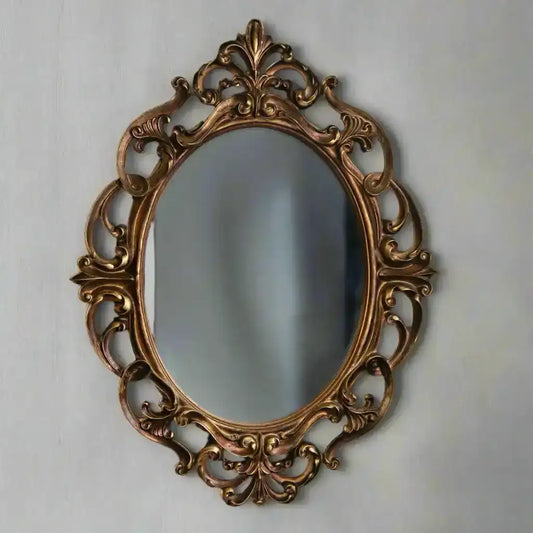 Decorative oval mirror with intricate gold frame on a light gray wall