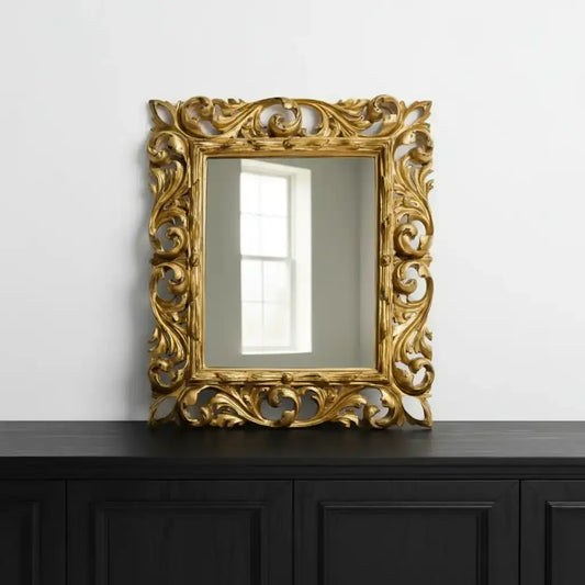 Decorative gold mirror with intricate patterns on a black cabinet against a white wall