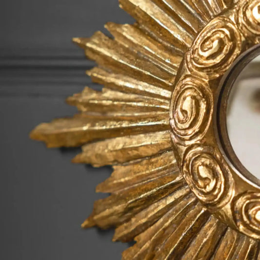 Close-up of a gold decorative mirror with intricate designs on a dark background