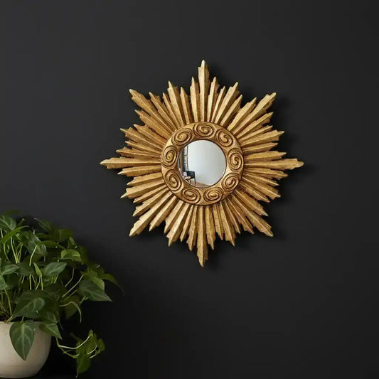 Decorative sunburst mirror on a black wall with a plant to the left.