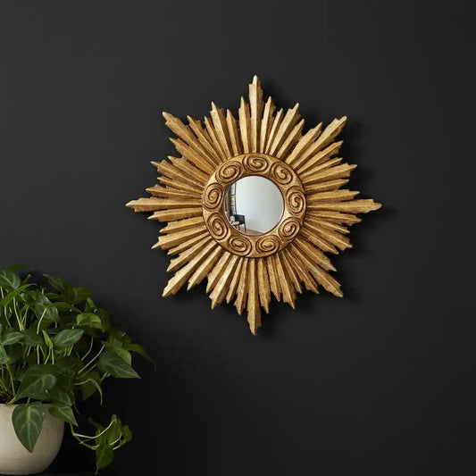 Decorative sunburst mirror on a black wall with a plant to the left.