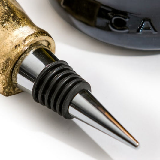 Close-up of a wine bottle stopper with a polished silver metal cone, a black ribbed rubber seal, and a brass-toned top section on a white background.
