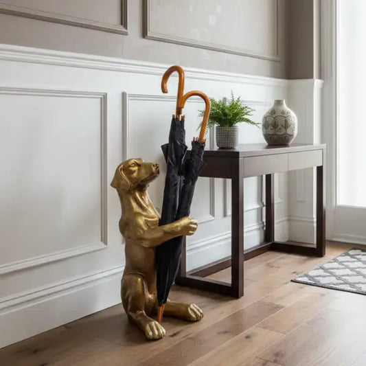 Gold dog-shaped umbrella stand holding a black umbrella in a room with wooden flooring and a small table.