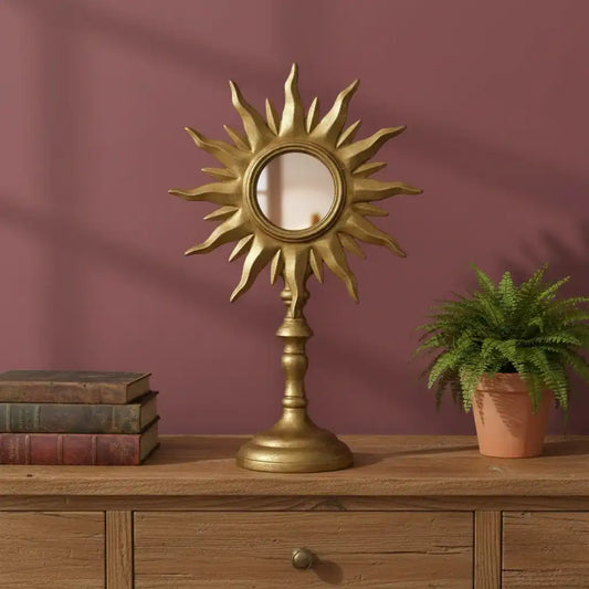 Decorative sun-shaped mirror on a wooden surface with books and a plant against a purple wall.
