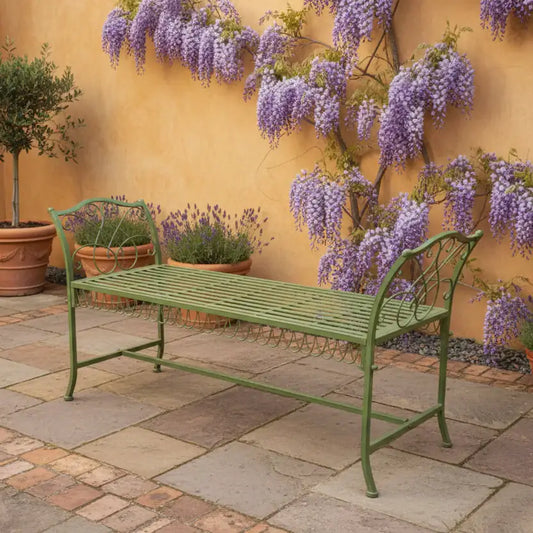Green metal bench in a garden setting with wisteria and potted plants.