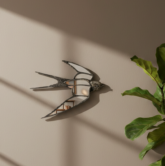 A decorative wall mirror shaped like a swallow, mounted on a beige wall. The mirror has a dark, textured frame and reflects a miniature living room scene.
