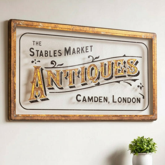 Vintage-style sign for 'The Stables Market Antiques, Camden, London' on a wall with decorative items below.