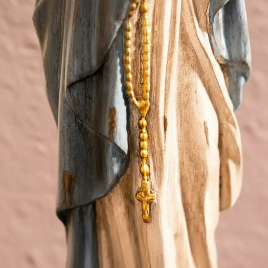 Gold rosary hanging on a wooden surface with a blurred background