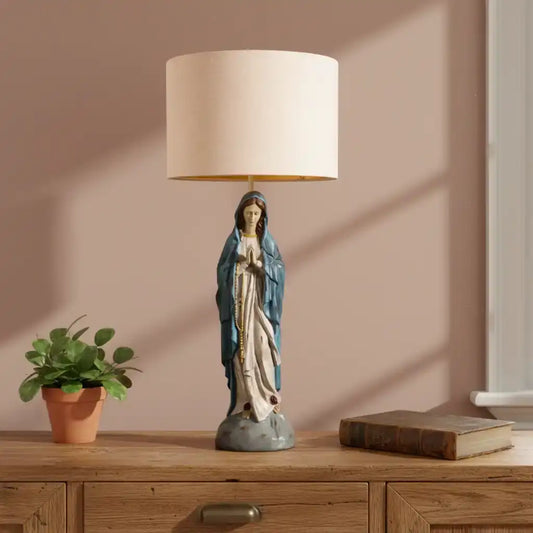 Table lamp with a figurine on a wooden surface next to a plant and book.