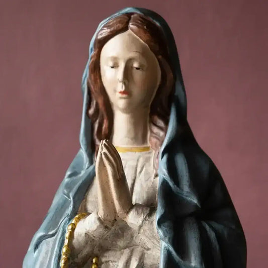 Statue of a woman in a blue hood with hands clasped, on a brown background