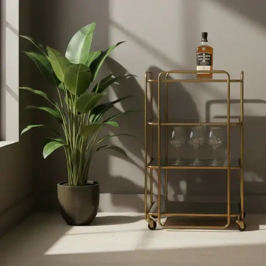 Gold bar cart with a bottle and glasses next to a potted plant in a sunlit room.