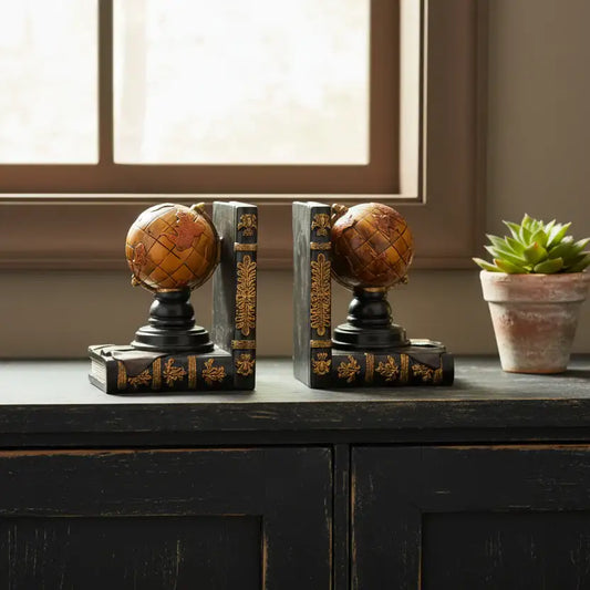 Decorative bookends shaped like globes on a wooden surface with a potted plant in the background.