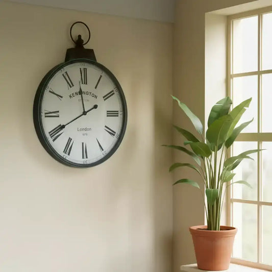 Decorative wall clock on a beige wall with a plant next to a window.