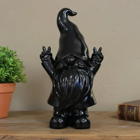 Black gnome figurine making peace signs on a wooden surface with a plant and book in the background.