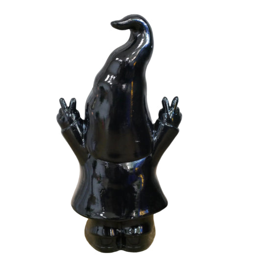 Black ceramic gnome figurine with a long hat on a wooden surface with a stone wall background