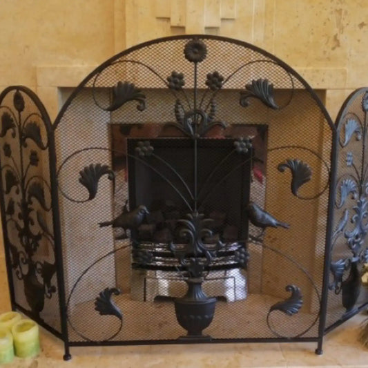 Decorative wrought iron fireplace screen with intricate designs in a room with beige walls.