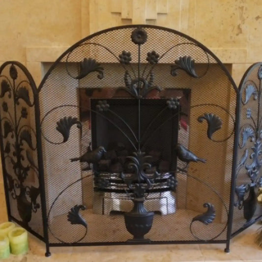 Decorative wrought iron fireplace screen with intricate designs in a room with beige walls.