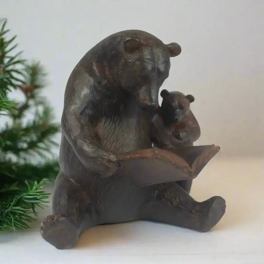 Bronze statue of a bear reading a book to a cub with a Christmas tree in the background
