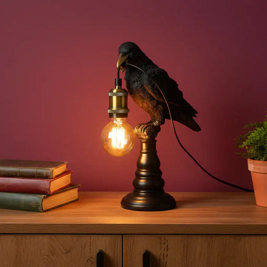 Decorative lamp with a bird design on a wooden surface against a red wall.