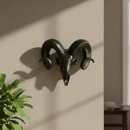 Decorative black ram's head wall mount on a beige wall with a plant in the foreground.