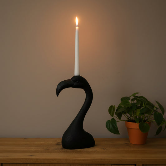 Black flamingo-shaped candle holder with a lit candle on a wooden surface.