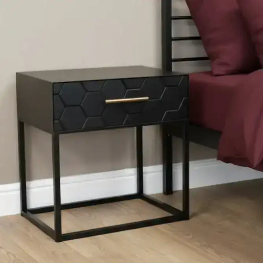 Black hexagonal patterned nightstand with gold handle next to a bed with burgundy bedding.