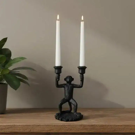 Black monkey-shaped candle holder with two lit white candles on a wooden surface.