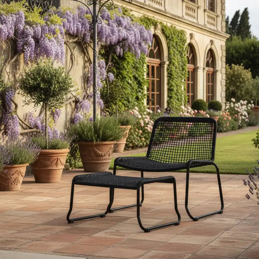 Black outdoor chair and ottoman on a patio with a garden and building in the background