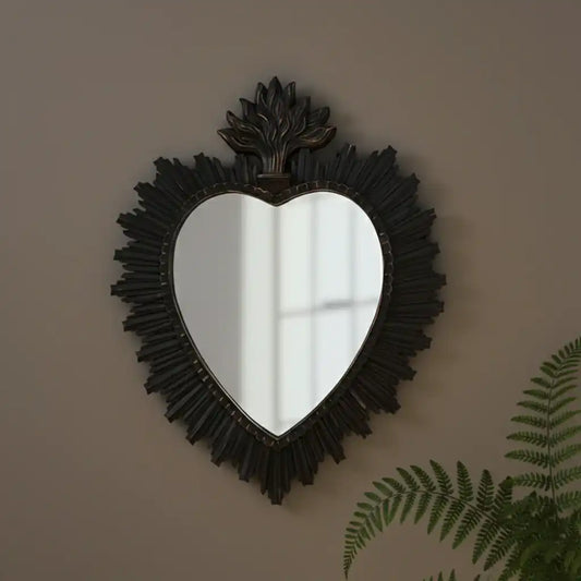 Heart-shaped mirror with decorative frame on a wall with a plant in the corner