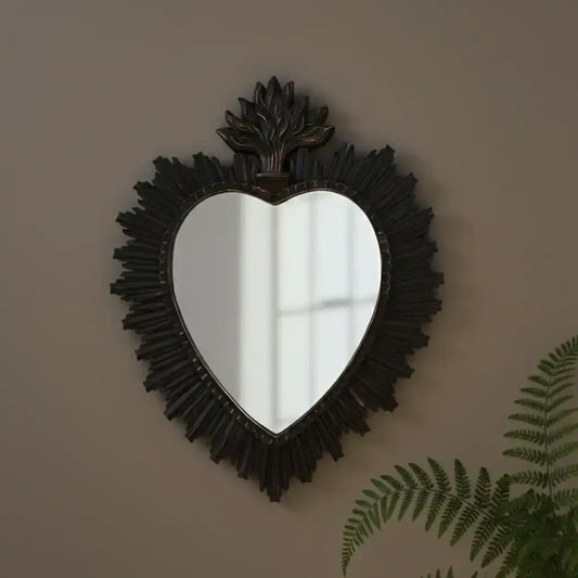 Heart-shaped mirror with decorative frame on a wall with a plant in the corner
