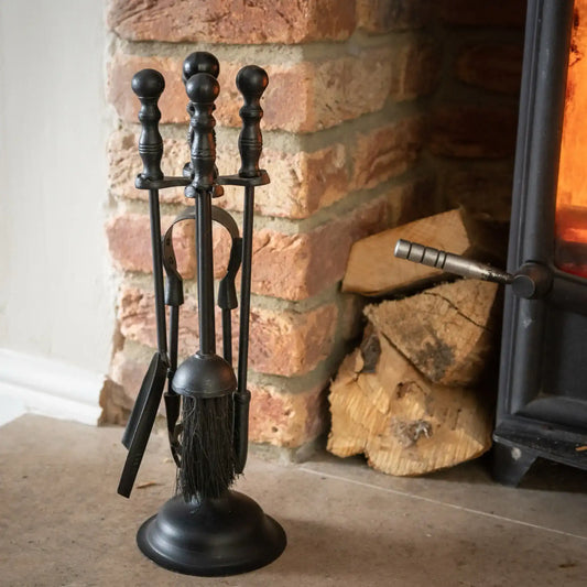 Black fireplace tool set in front of a brick fireplace with logs.