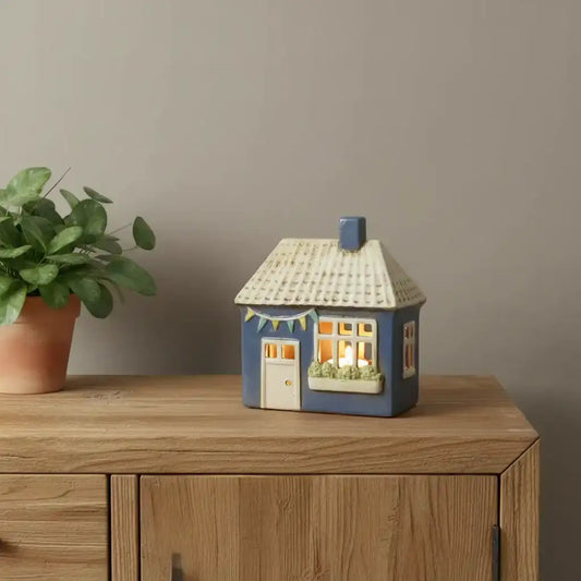 Decorative house-shaped lamp on a wooden surface with a plant beside it.
