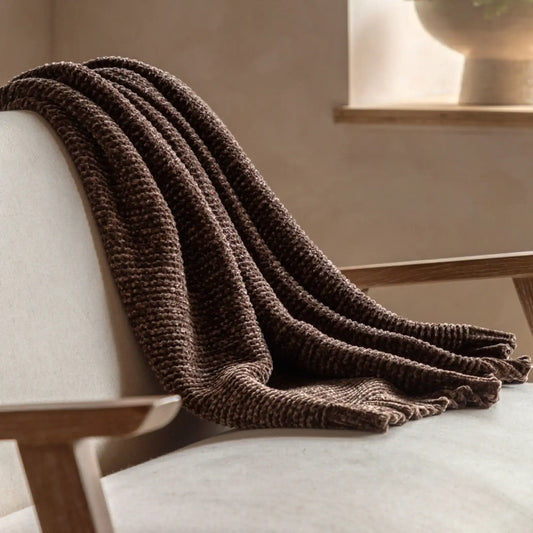 Brown knitted blanket draped over a light-colored sofa in a cozy room.