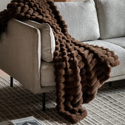 Brown textured blanket draped over a beige sofa in a living room setting.